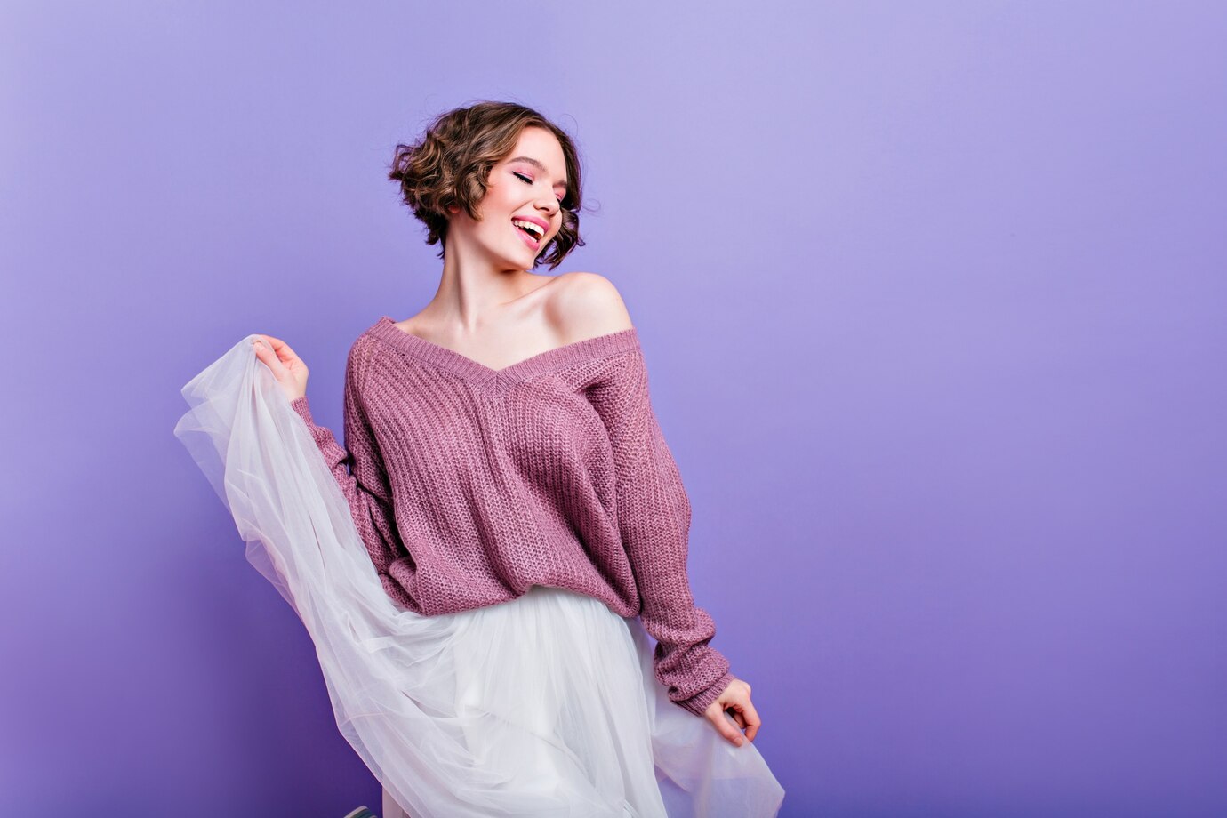 Enchanting woman with dark hair plays with long white skirt indoor portrait fashionable caucasian girl wears purple knitted sweater dancing with eyes closed 197531 7933